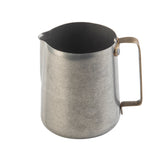 A stainless steel metal pitcher with a short spout and a sturdy, rectangular handle. The matte, slightly worn surface contrasts with the plain white background, making it ideal as a frothing cup for coffee or espresso drinks.