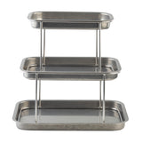 A 3-tier Sharing Tower with rectangular trays of decreasing size stacked vertically. Each tray is crafted from stainless steel with raised edges, supported by metal rods for a functional, industrial look. The empty trays reflect light beautifully.