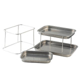 Three rectangular stainless steel trays and two metal wire racks form a 3-tier Sharing Tower. One rack elevates a tray for a tiered layout, while the other stands empty. The trays feature a simple design with rounded edges.
