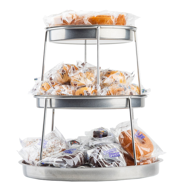 A 3-tier stainless steel sharing tower holds various individually wrapped pastries like donuts, cakes, and muffins. Each shelf displays an assortment in clear packaging with visible labels, all neatly arranged against a white background.