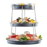 A stunning Sharing Tower features oysters, lobster tails, shrimp, mussels, and clams arranged on black trays with stainless steel supports, topped with lemon wedges and parsley over crushed ice. Perfect for a seafood feast.
