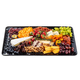 A black rectangular serving platter with assorted cheeses, sliced meats, fresh fruits, dried apricots, mixed nuts, pecans, crackers, and small containers of honey or mustard—all arranged in neat, colorful sections.