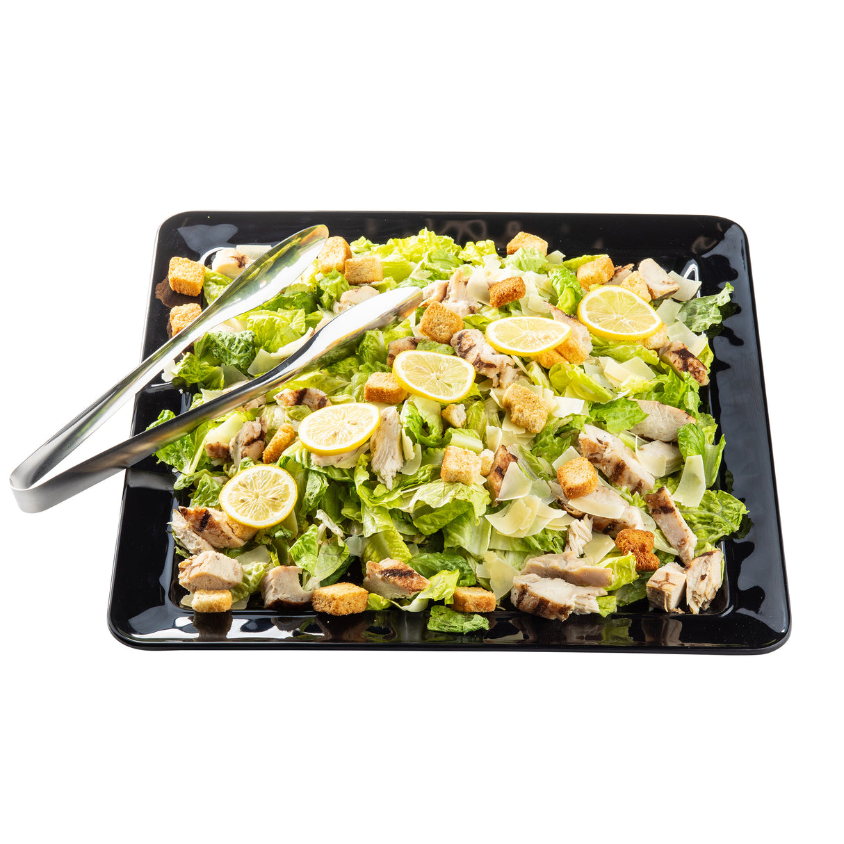 A square black Ridge Collection Serving Platter holds a Caesar salad with chopped romaine, grilled chicken, croutons, parmesan, and lemon slices. Metal tongs rest on the TableCraft melamine platter against a white background. Food is neatly arranged.