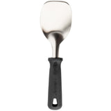 A metal spatula with a wide, slightly curved stainless steel blade and a black, ergonomic PerfectGrip handle featuring a hanging hole. The handle has a textured grip with “Pampered Chef” embossed on it. NSF certified for professional kitchens.
