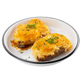 Two twice-baked potatoes are topped with golden melted cheese and chives, served on a TableCraft coupe bowl with a silver rim. The crispy skins are filled with creamy, piped filling, while the white background keeps the focus on this delicious dish.