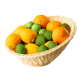 A white handwoven basket filled with a variety of citrus fruits, including whole oranges, lemons, and green limes, all arranged together on a white background.
