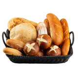 A handwoven black wicker basket, like the TableCraft 12135, filled with assorted breads—round rustic loaves, baguettes, pretzel rolls with salt and cross cuts, and small oval rolls—artfully arranged against a white background.
