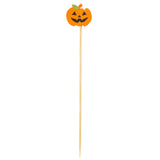 A wooden skewer, like the TableCraft 12141 Halloween bamboo picks, is topped with a smiling orange jack-o-lantern made of paper or felt. The pumpkin features black triangle eyes and nose, a jagged mouth, and a small green leaf on its stem.