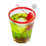 A glass filled with bright green liquid and ice, garnished with a red cherry on a bamboo snowflake pick and another cherry inside. The rim is coated with red sugar, while the white background enhances its festive, vibrant appeal.