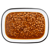 A rectangular white enamel serving pan with a black rim, filled with baked beans in a rich, reddish-brown sauce. The beans are evenly distributed, with some sauce pooling around the edges. Photographed from above on a white background.