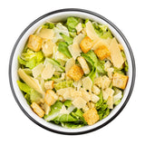 A white TableCraft serving bowl filled with Caesar salad, featuring chopped romaine lettuce, golden croutons, and wide shavings of parmesan cheese, all arranged neatly on a white background.