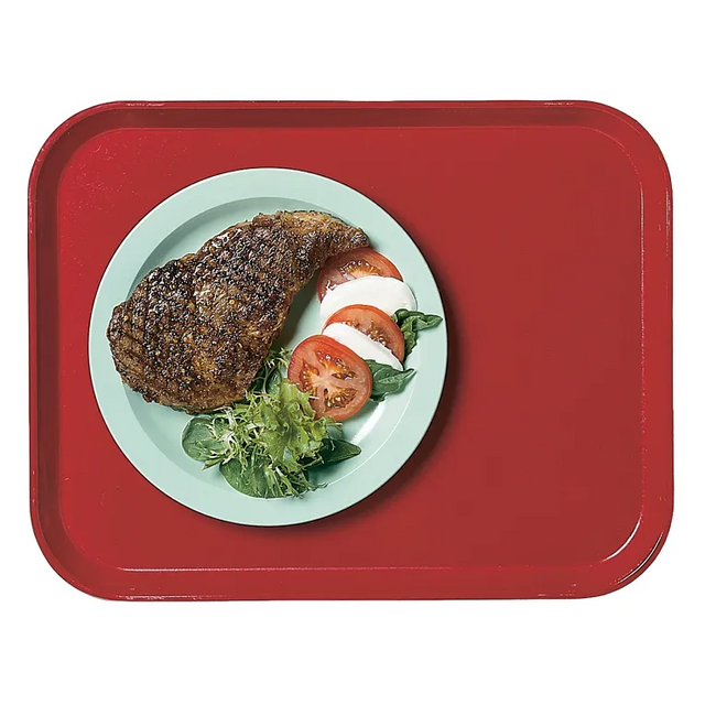 A green plate on a Camlite Tray holds a grilled steak, slices of fresh tomato, mozzarella, and leafy greens arranged beside each other. The durable fiberglass tray is dishwasher safe and vibrant in red when viewed from above.