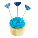 A vanilla cupcake with bright blue frosting is topped with three decorative picks, each featuring a blue menorah cutout. The cupcake is isolated on a white background.