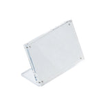 A TableCraft Acrylic Sign Holder stands at an angle with a rectangular display area, supported by a transparent L-shaped base. Four small inset magnets are visible at the corners, securing the front and back panels together. The background is white.