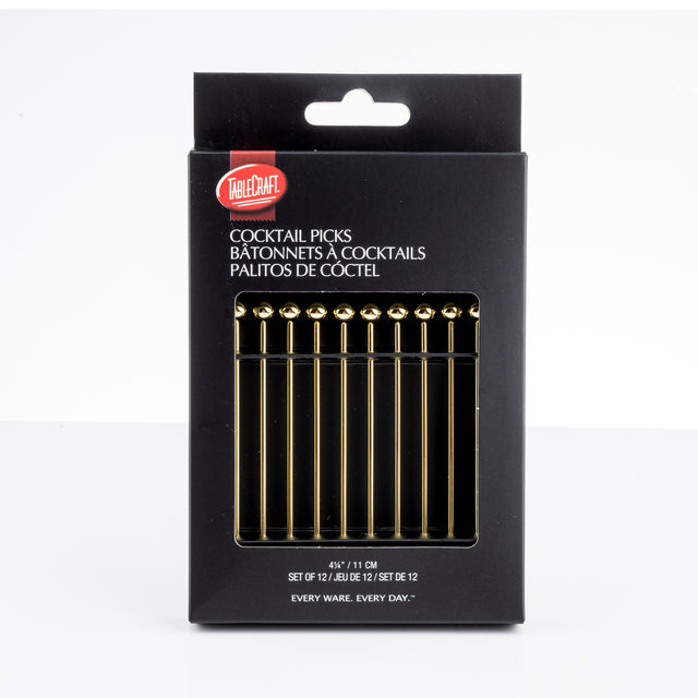 A black box of TableCraft cocktail picks is shown upright. The package displays 12 gold stainless steel picks with spherical tops visible through a window. White text on the box provides product name and details in English, French, and Spanish.