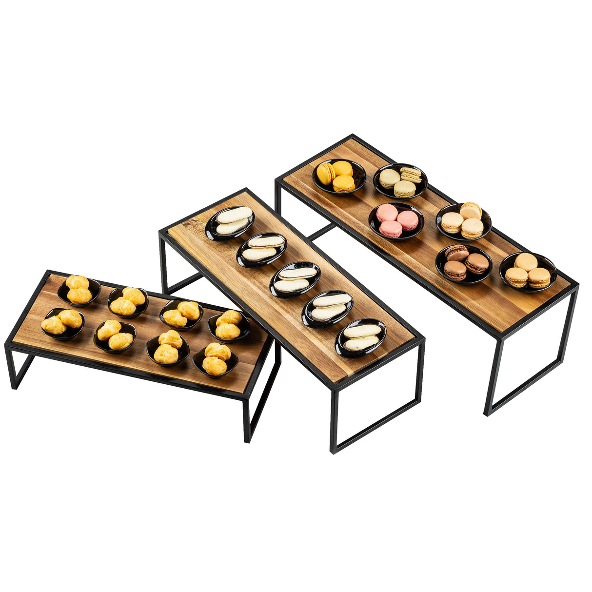 Three rectangular Acacia wood risers with black powder coated steel frames are arranged at different heights. Each stand holds several black plates, displaying assorted pastries including macarons and cream-filled buns, neatly organized in rows. The background is white.