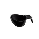 A black ceramic cup with an asymmetrical, organic shape and a wide, curved handle sits on a white background. Its modern, minimalist design and smooth surface make it versatile enough to use as a unique sauce boat.