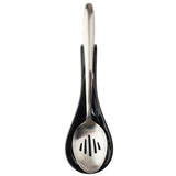 A stainless steel slotted spoon rests in a glossy black melamine TableCraft Spoon Rest, both items seen from above on a white background. The centered handle and slots in the spoon’s bowl are neatly cradled by the holder.