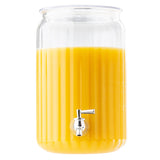 A large, clear acrylic beverage dispenser, with vertical ridges and a metal spigot near the bottom, holds about 2 gallons of orange juice up to three-quarters full. The plain white background keeps the focus on the dispenser.