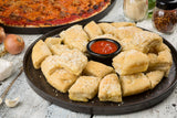 A round melamine platter from the TableCraft Lunara Collection holds golden, fluffy garlic bread bites sprinkled with parmesan cheese, arranged around a small cup of marinara sauce on a rustic white table.