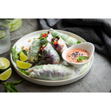 Four fresh vegetable spring rolls sit on a round white tray, with lime wedges, mint leaves, and chopped peanuts on the side. A small bowl of pink dipping sauce sprinkled with black sesame seeds completes this vibrant Europa Collection Serving Tray display.