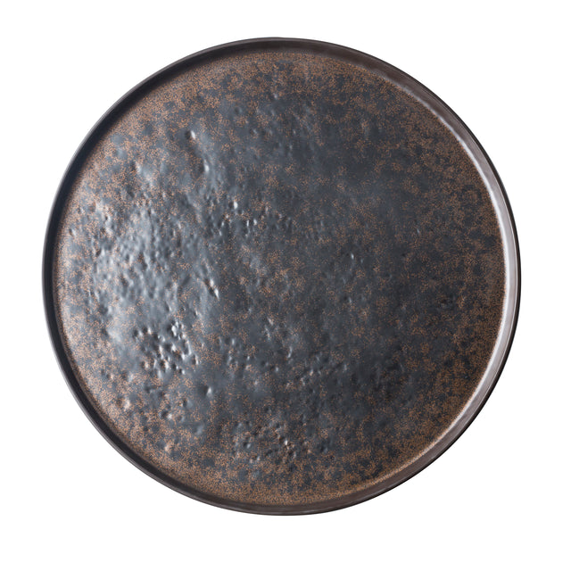 A round serving tray with a textured, uneven surface and mottled pattern. This ceramic platter features black and brown tones for a rustic, earthy look. The plain white background highlights the design of the plate.