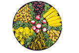 A Lunara Collection platter holds sections of olives, pickles, yellow peppers, kalamata olives, pickle spears, and kale. Red radishes with white centers are arranged in the middle, creating a colorful vegetable and pickle assortment.