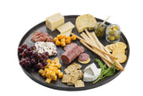 A round serving platter holds assorted cheeses, salami, prosciutto, crackers, breadsticks, grape tomatoes, green olives in a jar, a basil sprig, red grapes, and cubed cheese—all arranged neatly with small jars and a cheese knife. White background.