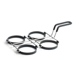 A metal kitchen utensil with four non-stick egg rings arranged in a grid and connected by metal bars, featuring a handle with a black grip. Designed for cooking evenly shaped eggs or pancakes. Dishwasher safe. The background is white.