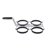 A metal kitchen tool with a black handle and four round, non-stick egg rings arranged in a square, connected by metal bars. It’s designed for cooking perfectly round eggs or pancakes on a stovetop and is dishwasher safe.