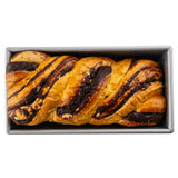 A rectangular Non-Stick Bread Pan holds a baked chocolate babka inside. The golden-brown, braided bread features thick, dark chocolate swirls and glossy patches, creating a rich, marbled pattern on the loaf’s surface.