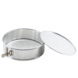A round, aluminum springform pan with a removable flat lid is shown. The pan features a durable latch on the side for easy opening and closing. The lid is positioned to the right, resting slightly tilted and revealing the empty interior.