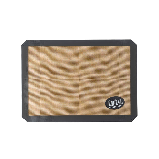 A half size silicone baking mat with a tan center and black border. The mat features a textured surface and the TableCraft logo printed in white on a black oval in the lower right corner. Background is plain white.