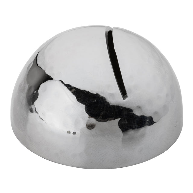 A shiny, stainless steel dome-shaped metal object with a silver hammered pattern and a single narrow slit on top, resembling a modern, minimalist coin bank or sculptural money box. The surface reflects light and surroundings.
