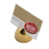 A gold stainless steel card holder with a hammered pattern holds a business card upright. The card displays TableCraft Products Company and address details, featuring a bold red TableCraft logo. The background is plain white.