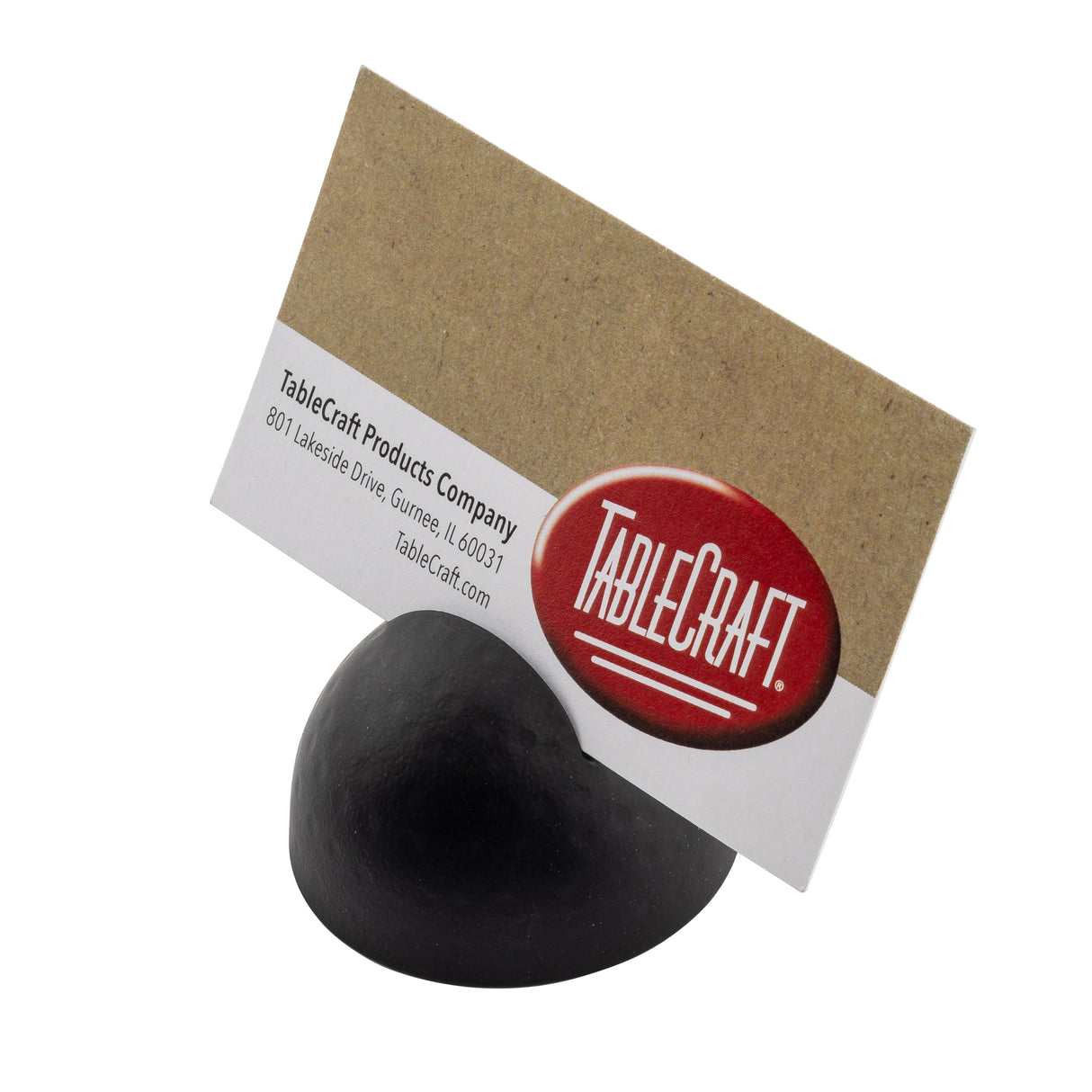 A black powder coated half-sphere card holder with a subtle hammered pattern displays a kraft paper business card at an angle. The card features the TableCraft Products Company name, red and white logo, and company address. Background is plain white.