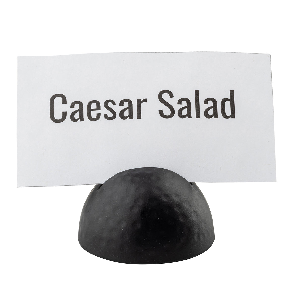 A white card with bold black text reads Caesar Salad. The card is held upright by a small, round, black powder coated card holder with a hammered pattern against a plain white background.