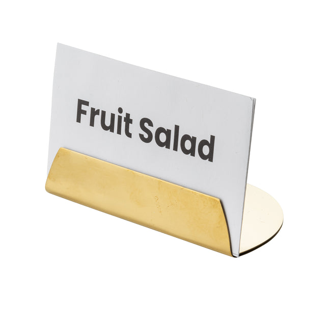 A white card labeled Fruit Salad in bold black letters is held upright by a gold coated stainless steel TableCraft Products Half Moon Card Holder. The background is plain white, and the card and holder are viewed at a slight angle from the front.