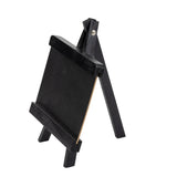 A small, black TableCraft wooden easel stands on three legs, holding a blank rectangular chalkboard vertically. The easel and board rest on a white background, supported by a metal screw at the top hinge.