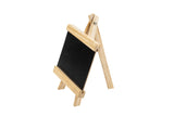A small black chalkboard serves as a tabletop board sign, held upright on a light wood easel with three legs and a sturdy frame. The background is white, and the blank chalkboard invites creativity.