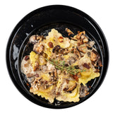 A black melamine serving plate holds square ravioli topped with creamy mushroom sauce, sautéed mushrooms, crispy bits, and thyme. Black pepper speckles the sauce, giving the pasta a rustic, gourmet look on this elegant platter.