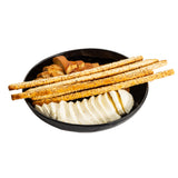 A black Melamine Serving Bowl from the Ridge Collection contains several thin breadsticks, round slices of white cheese, and a swirl of brown bread, all arranged neatly and isolated on a white background.