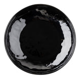A round, glossy black TableCraft plate seen from above. The melamine surface has subtle reflections and wavy edges, giving it a slightly irregular, hand-crafted appearance. The plate is empty and isolated on a white background.