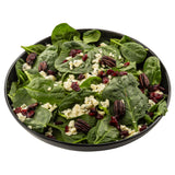 A black TableCraft melamine serving bowl filled with fresh spinach leaves, topped with crumbled blue cheese, candied pecans, and dried cranberries. The white background makes the vibrant salad ingredients stand out beautifully.