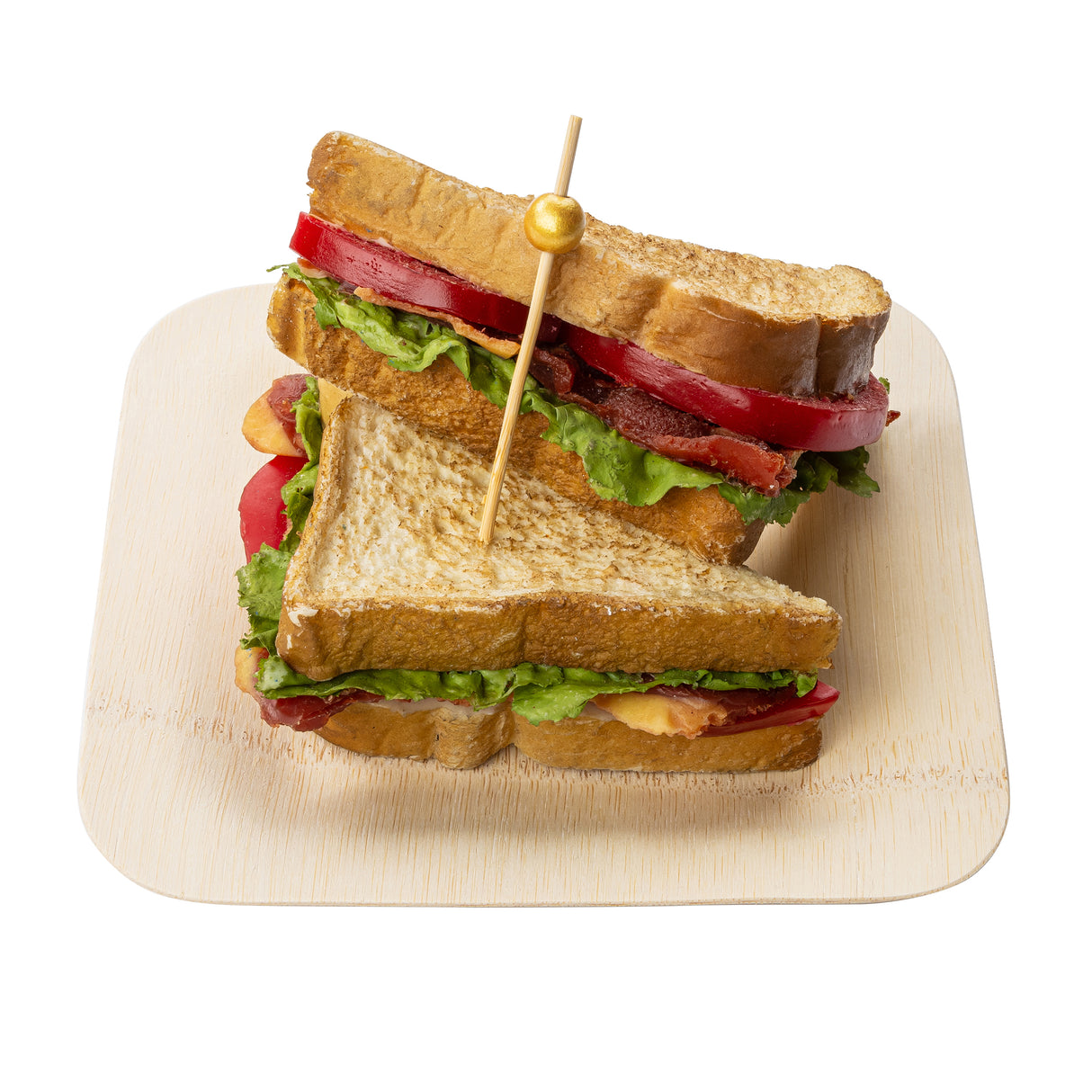 A sandwich cut in half is stacked on a light wooden plate. Filled with lettuce, tomato slices, crispy bacon, and toasted bread, it’s held together with elegant gold picks. The white background makes the sandwich and plate stand out clearly.