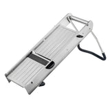 A stainless steel mandoline from the TableCraft Mandoline Slicer Set is shown at an angle, resting on its foldable black-and-silver stand. The slicer features a flat, ridged surface with an exposed blade in the center for slicing vegetables.