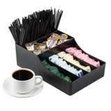 A TableCraft Coffee Condiment Organizer made of durable polypropylene holds black coffee stirrers, single-serve creamers, and packets of sugar and sweeteners. In front sits a white cup filled with black coffee on a matching saucer.