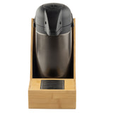 A stainless steel airpot with a black lid sits upright in a bamboo Single Airpot Rack. The stand features a stainless steel drip tray at the base, directly in front of the spout, and is designed for easy coffee dispensing.