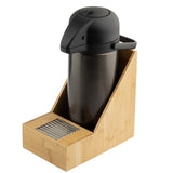 A stainless steel airpot with a black lid and handle sits in a bamboo Single Airpot Rack. The angled holder features a front compartment with stir sticks and pairs perfectly with a stainless steel drip tray for convenient beverage service.