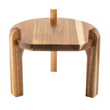 A small, round acacia wood stool with three thick, curved legs and a smooth, natural finish. One leg extends vertically above the seat, giving it a simple, modern edge—perfect as a minimalist glass beverage dispenser stand.
